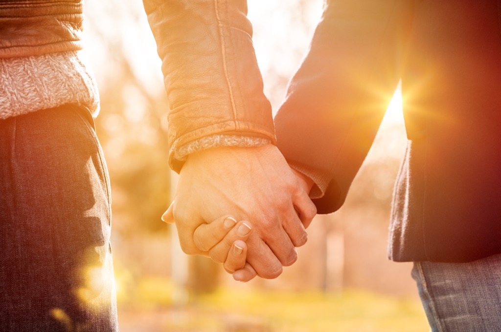 closeup of a couple holding hands outside during sunset
