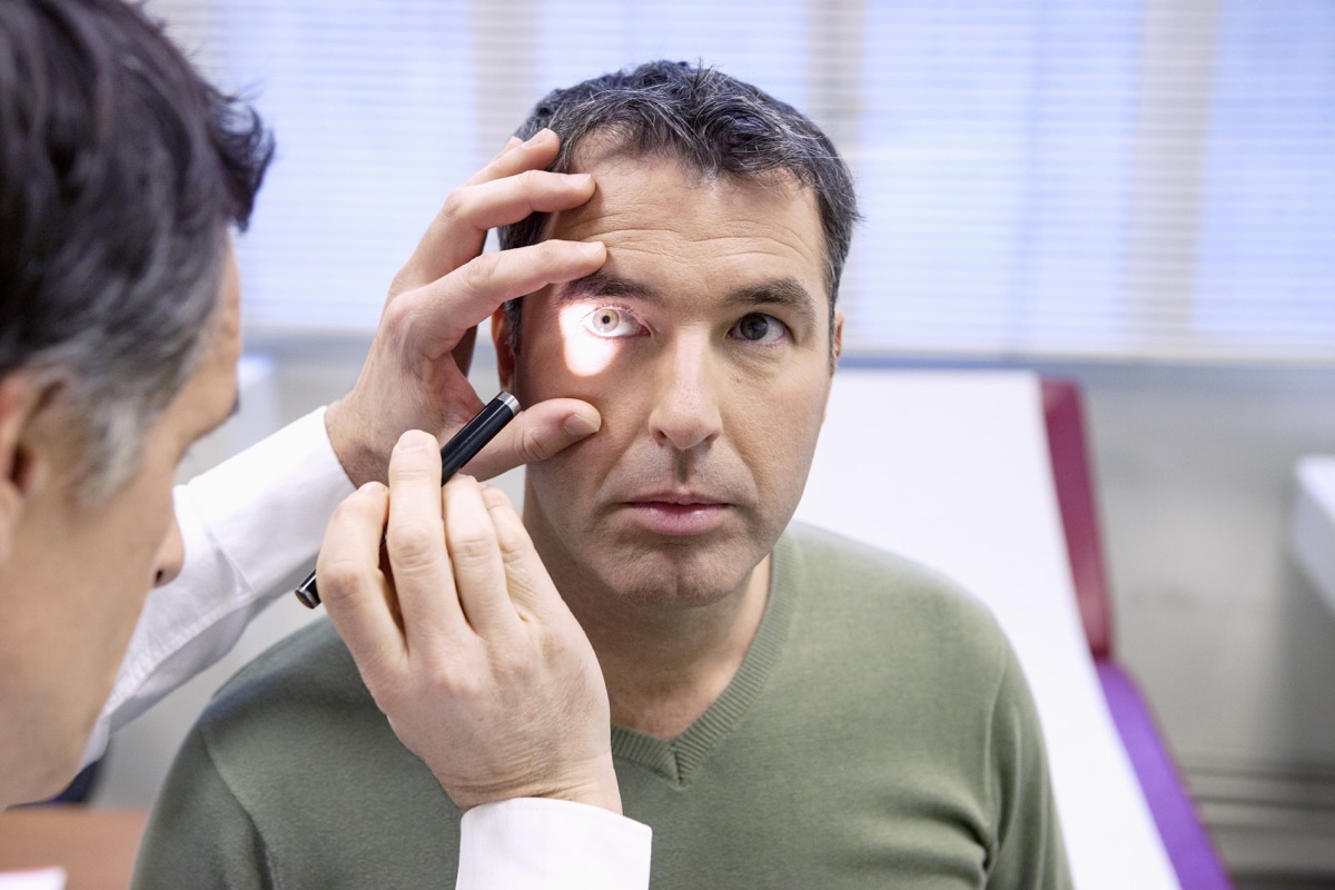 Male optometrist shining a pen light into the eye of a male patient