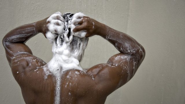 black man with his back to camera shampooing his hair in the shower