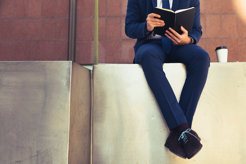 man on a ledge reading a book in a suit - how to dress over 50