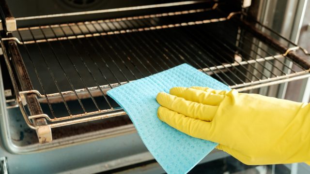 hand in yellow glove cleaning oven with blue sponge
