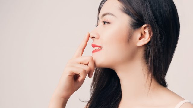 Young beautiful Asian woman with smiley face and red lips touching her nose