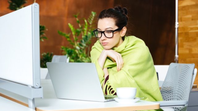 shivering woman in office with blanket, signs your cold is serious