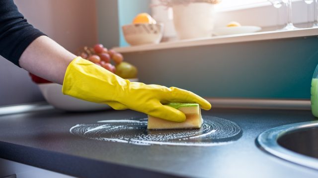 white person wearing gloves cleaning counters with sponge