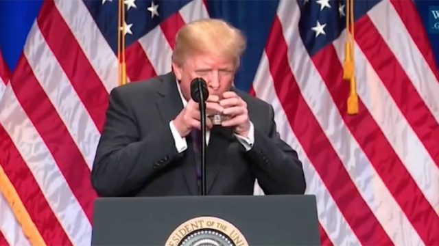 trump uses two hands to hold glass of water