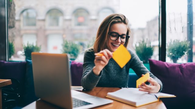 a woman sitting in front of a laptop in a cafe putting sticky notes in a book
