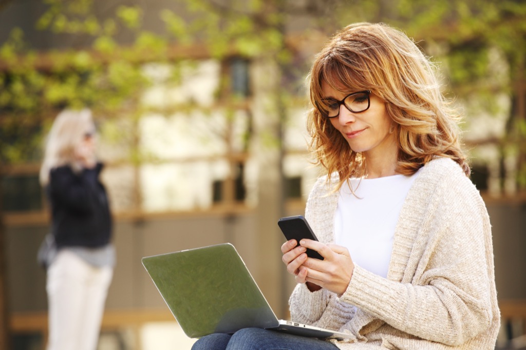 woman working on smartphone and laptop computer outside dating over 50