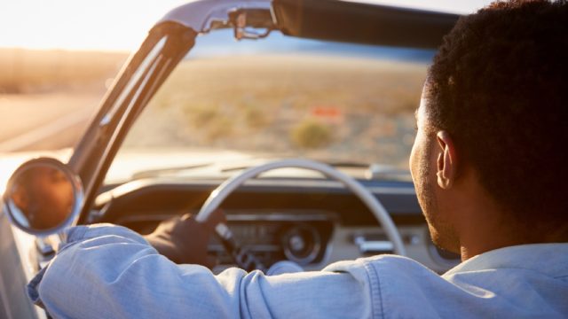 portrait from behind of black man driving a convertible in the desert, changes over 40