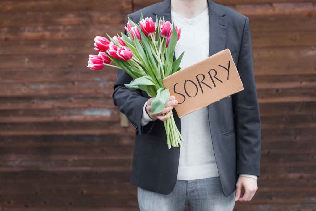 man holding flowers and sign that reads sorry