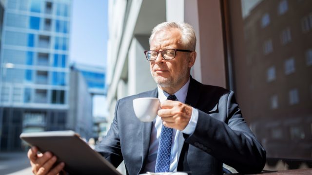 an older businessman ponders retirement while looking at an ipad, office etiquette