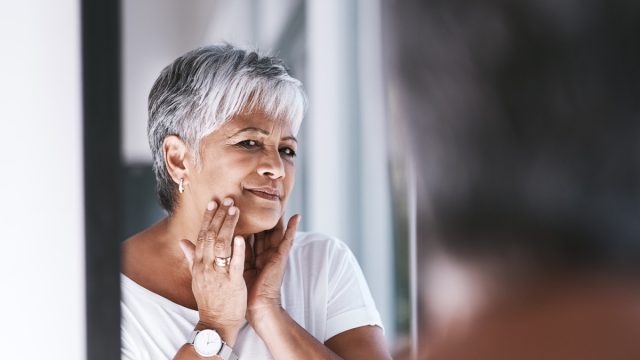 Mature woman touching her face with her hands while looking at her reflection in a mirror