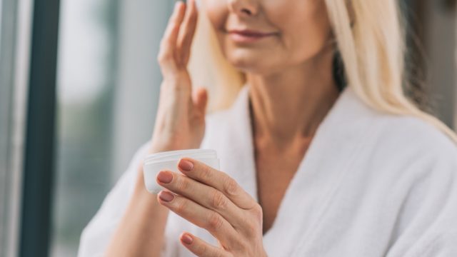 mature woman applying face cream in white robe