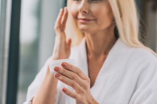 mature woman applying face cream in white robe
