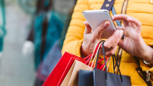 closeup of shopper in yellow coat with bags and phone in hand