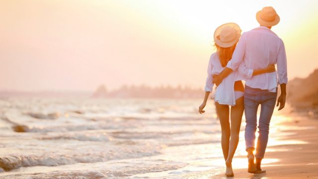 couple wearing hats walking on a beach at sunset - money can't buy happiness