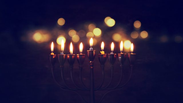 a lit menorah in darkness - hanukkah traditions