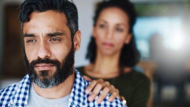 Shot of a woman comforting her distraught husband at home by putting her hand on his shoulder