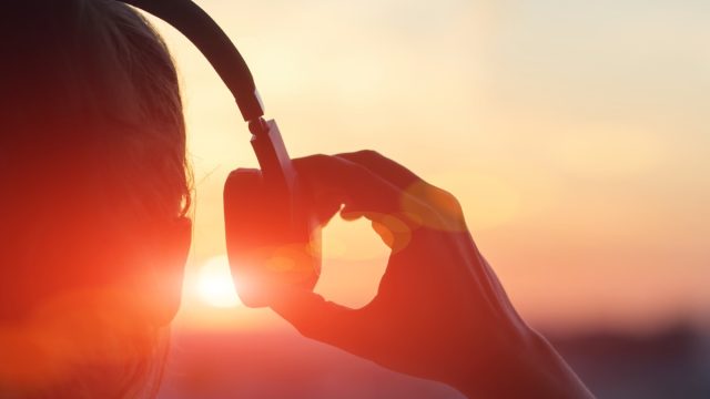 woman putting on over-ear headphones at sunset - sound facts