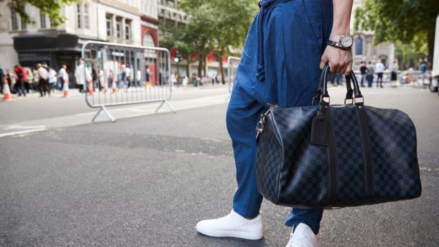 Waist down view of a man in blue trousers holding a bag