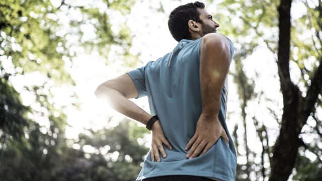 Man holds lower back in pain at a park