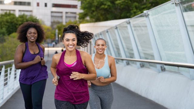 Curvy multiethnic young women jogging together on city bridge