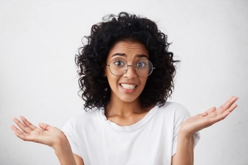 woman wearing glasses and shrugging, looking contrite