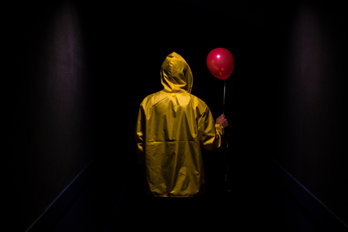 Hooded yellow figure with red balloon in dark creepy corridor 