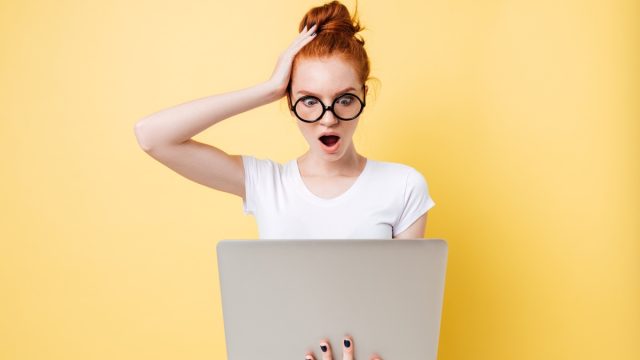shocked woman with red hair holding a laptop against an orange background