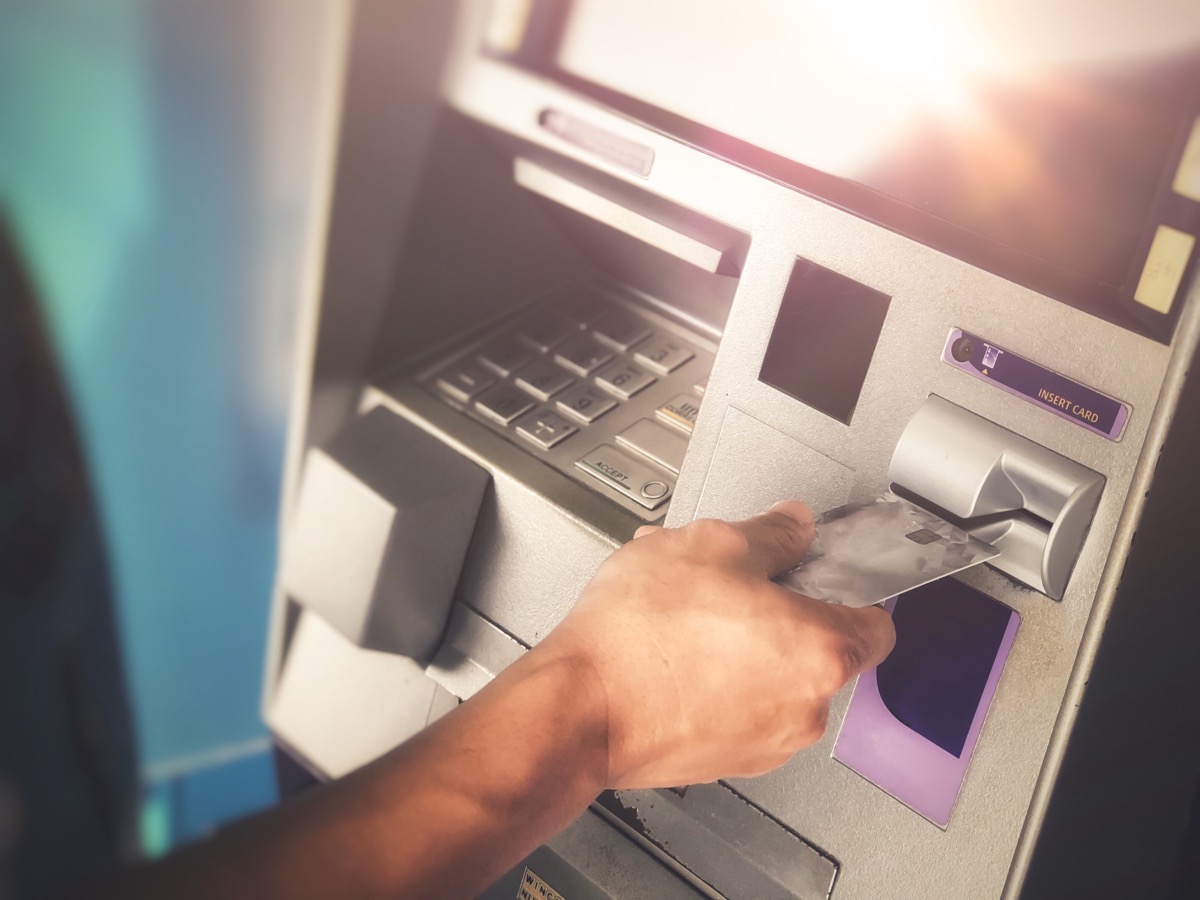Man’s hand inserting ATM credit card into bank machine to transfer money or withdraw - Image