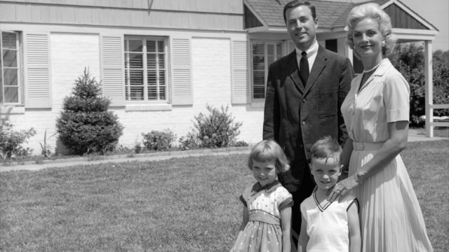 1960s suburban family in black and white photo standing in front of huge suburban home