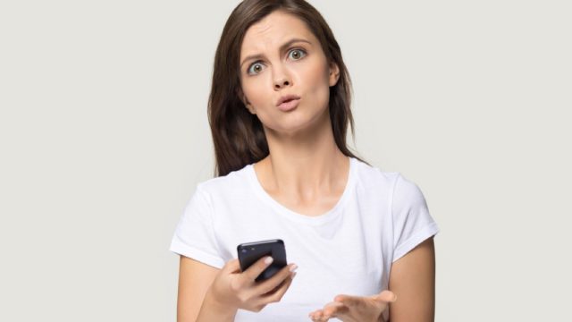 woman holding phone and looking confused