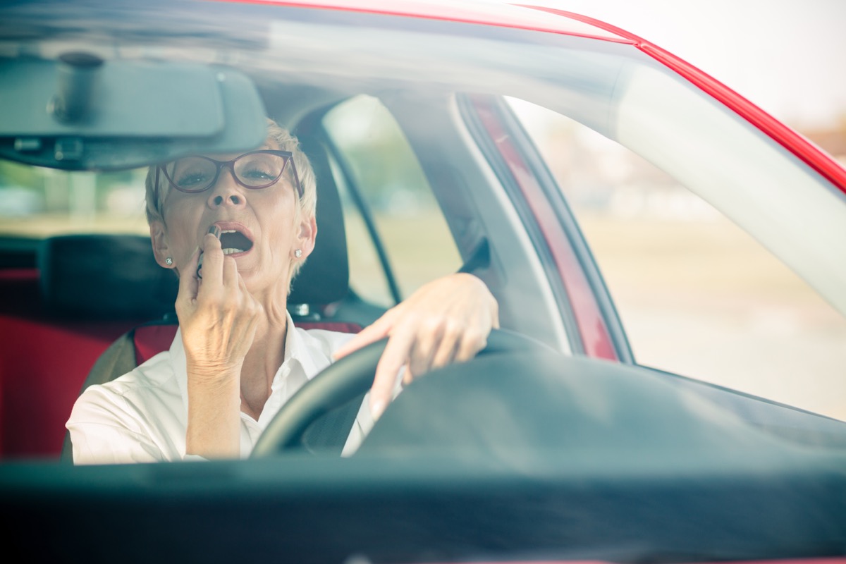 woman stopped at red light with short grey hair puts on lipstick