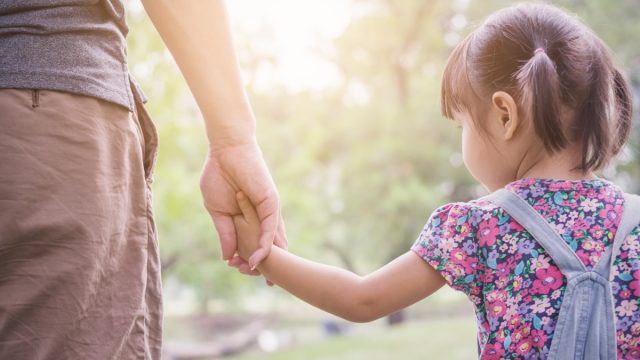Closeup from behind of dad and young Asian daughter holding hands, stay-at-home dad affects marriage
