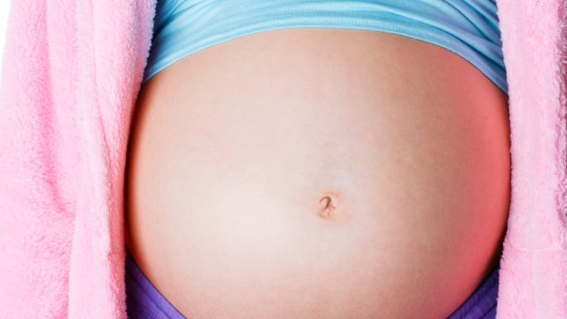 Closeup of pregnant teen belly with cropped shirt and pink sweater, what it's like being a teen mom