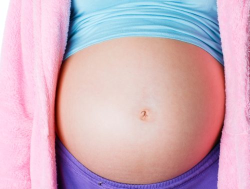 Closeup of pregnant teen belly with cropped shirt and pink sweater, what it's like being a teen mom