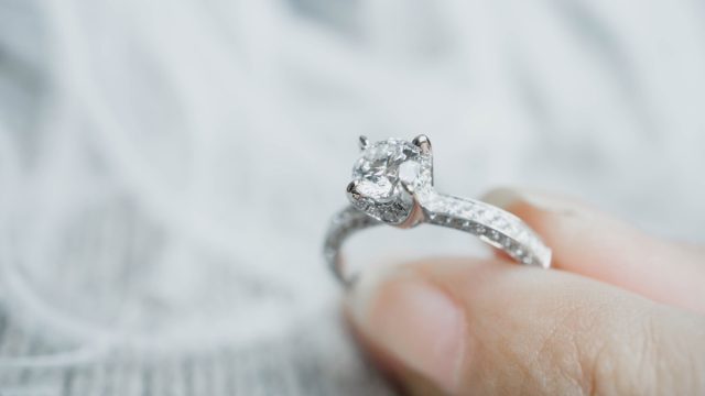 Closeup of woman's fingers holding engagement ring, postpone wedding