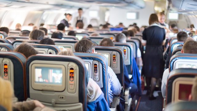 a flight attendant walks down the aisle of a crowded airplane