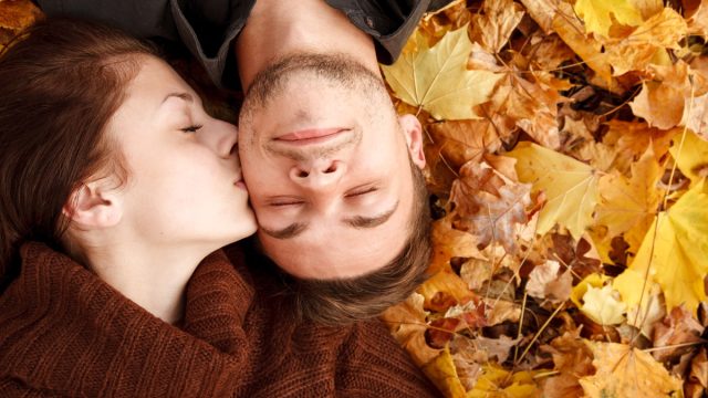 woman kissing man on the cheek while laying down in the foliage - romantic fall date ideas