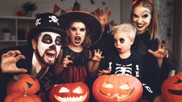family in halloween costumes standing in front of jack o'lanterns