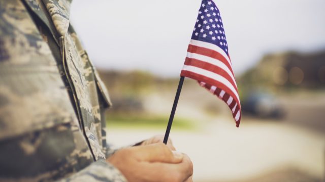 military man holding american flag - veterans day quotes