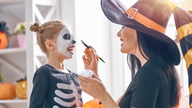 Mother dressed as witch painting skeleton makeup on little girl