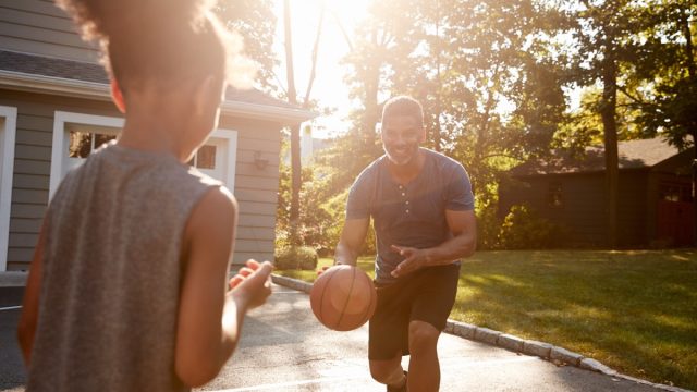 father and child playing basketball in suburbia