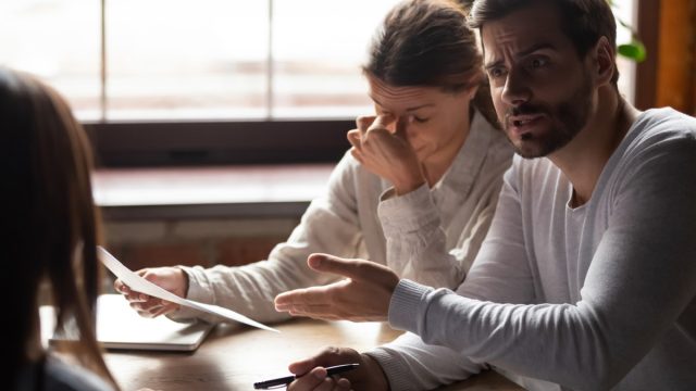 young white woman pinching between her eyes in frustration while young white male colleague yells at a woman