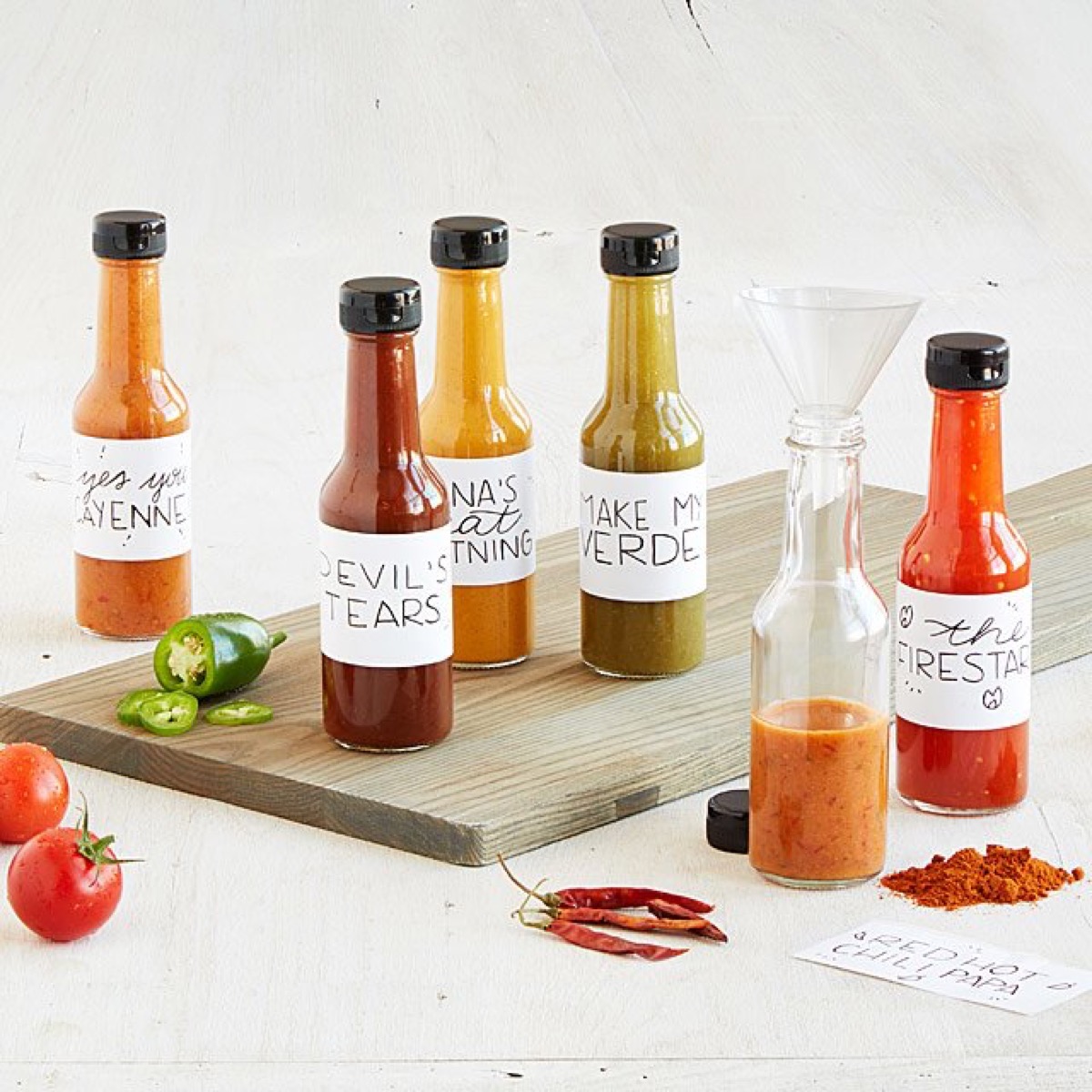 multi colored bottles of hot sauce on wooden cutting board