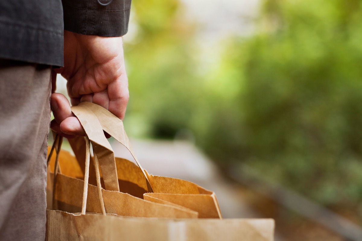 close up of man's hand holding the handle of a paper grocery bag