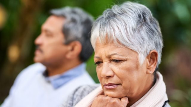 Shot of a senior woman of color looking upset with her husband in the background