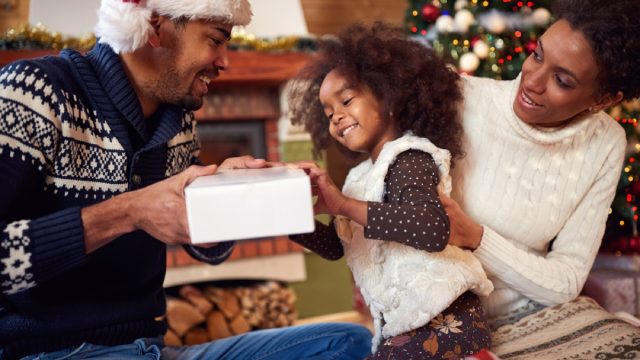 black man and woman in santa hats with little girl opening gifts