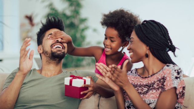 young black woman and man opening christmas gift in red and white box with young daughter