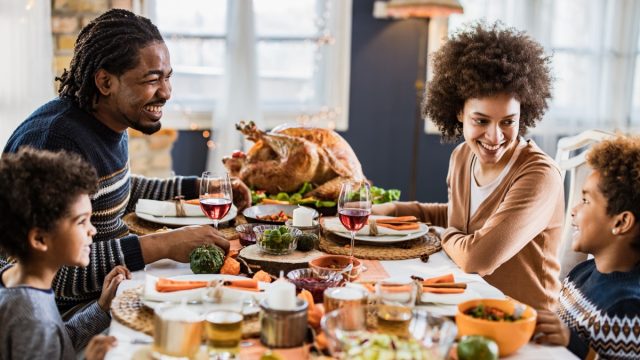 Happy black family talking during Thanksgiving meal at dining table.