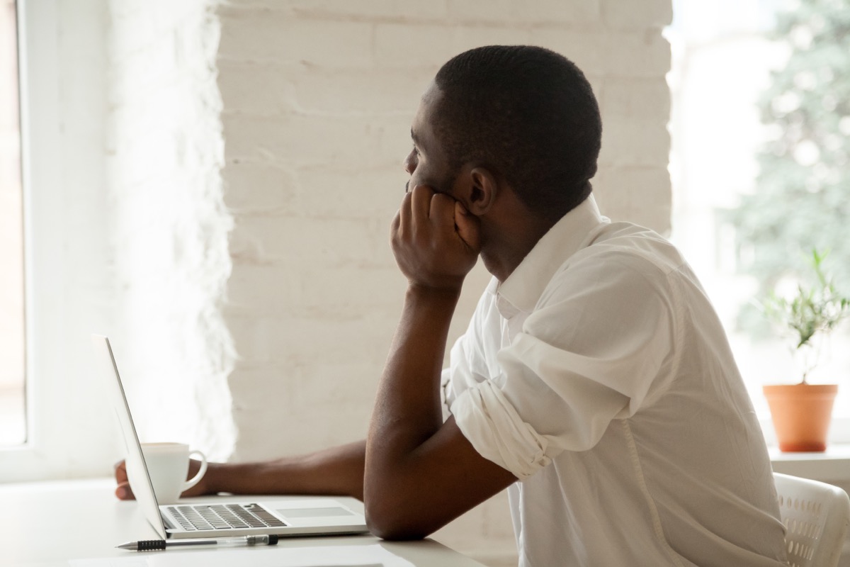 Man sitting at his desk with laptop and coffee, looking out the window
